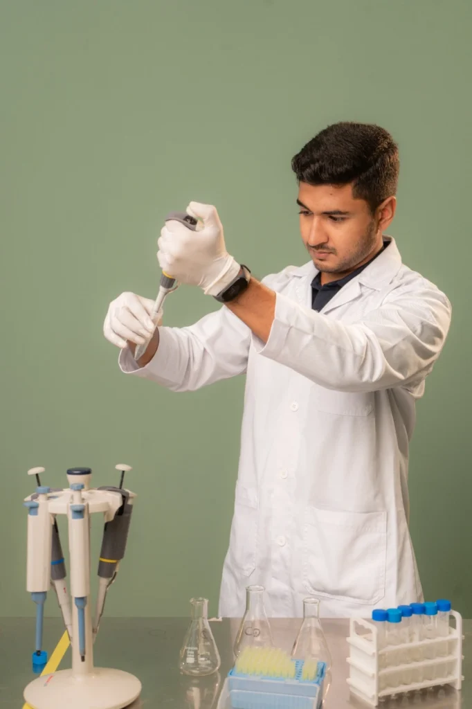 Scientist in a white lab coat and gloves uses a micropipette at a lab bench.