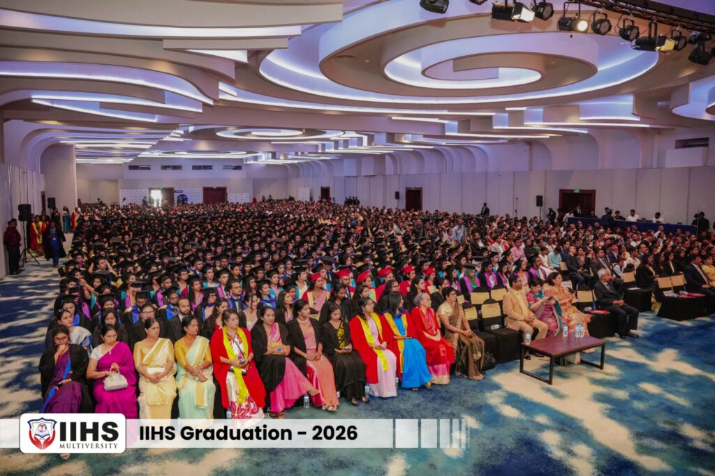 Large graduation ceremony in a spacious hall; rows of graduates in caps and gowns sit alongside formally dressed attendees, with a banner reading 'IIHS Graduation – 2026' at the front.